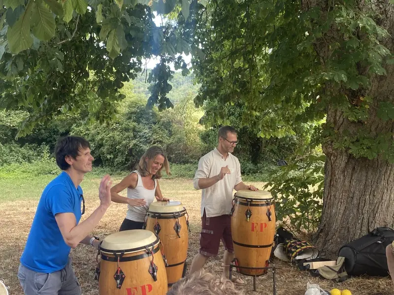 Trois personnes jouant des percussions sous un arbre